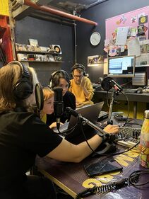 four young persons sitting in front of a sound table in a radio booth